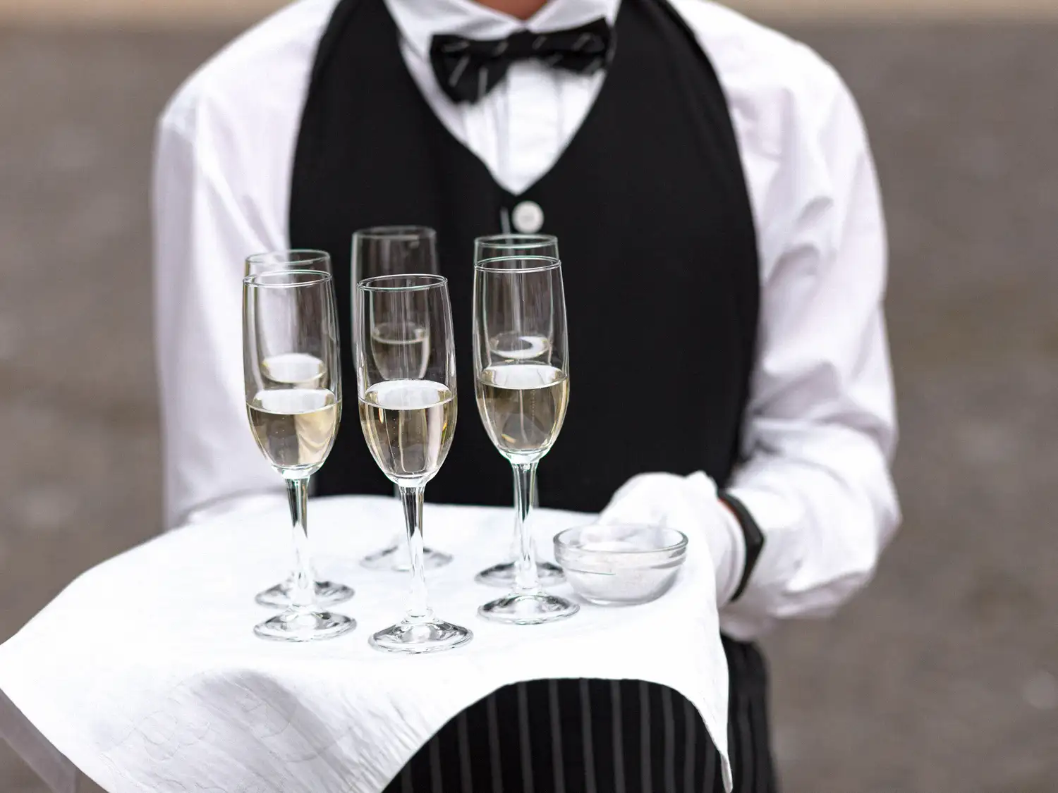 Butler in white gloves and a black waistcoat holding a tray of champagne flutes on a white napkin