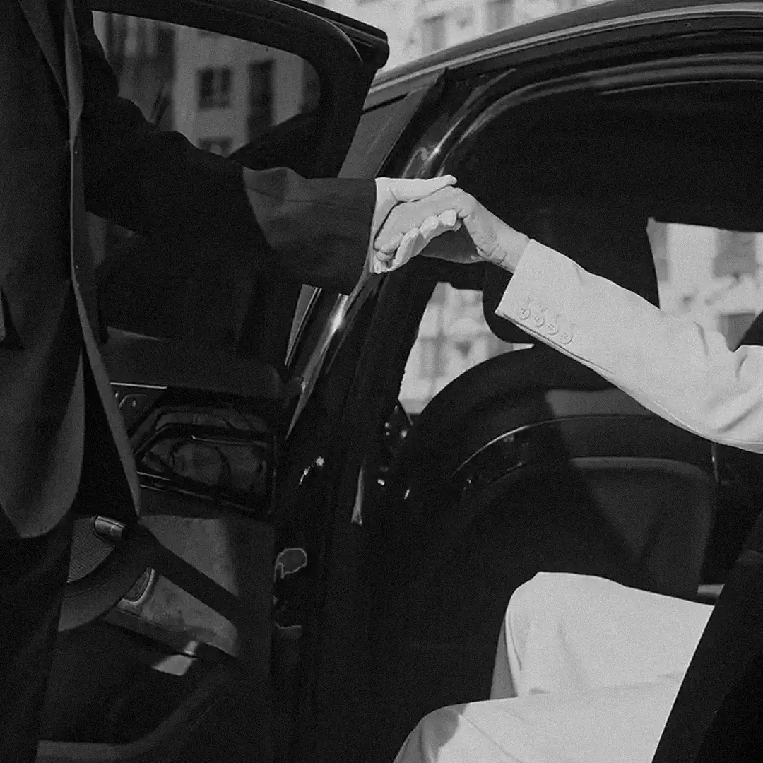 Chauffeur’s hand helping a passenger step out of a black car, in black and white