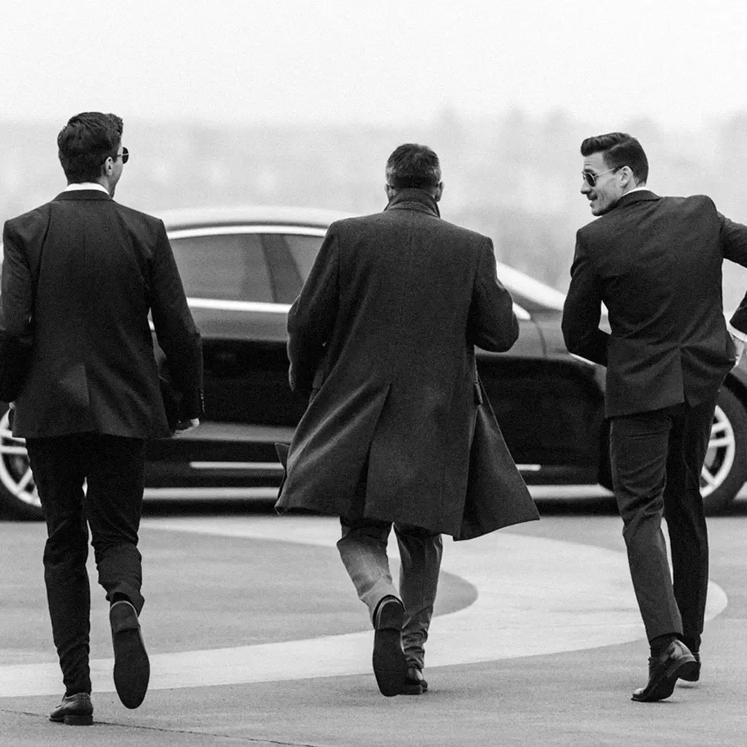 Three men in dark suits and coats walking towards a black car, illustrating private security service