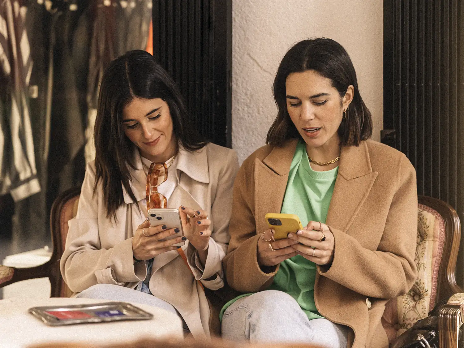 Two women in tailored coats checking their phones while planning a day with a private concierge